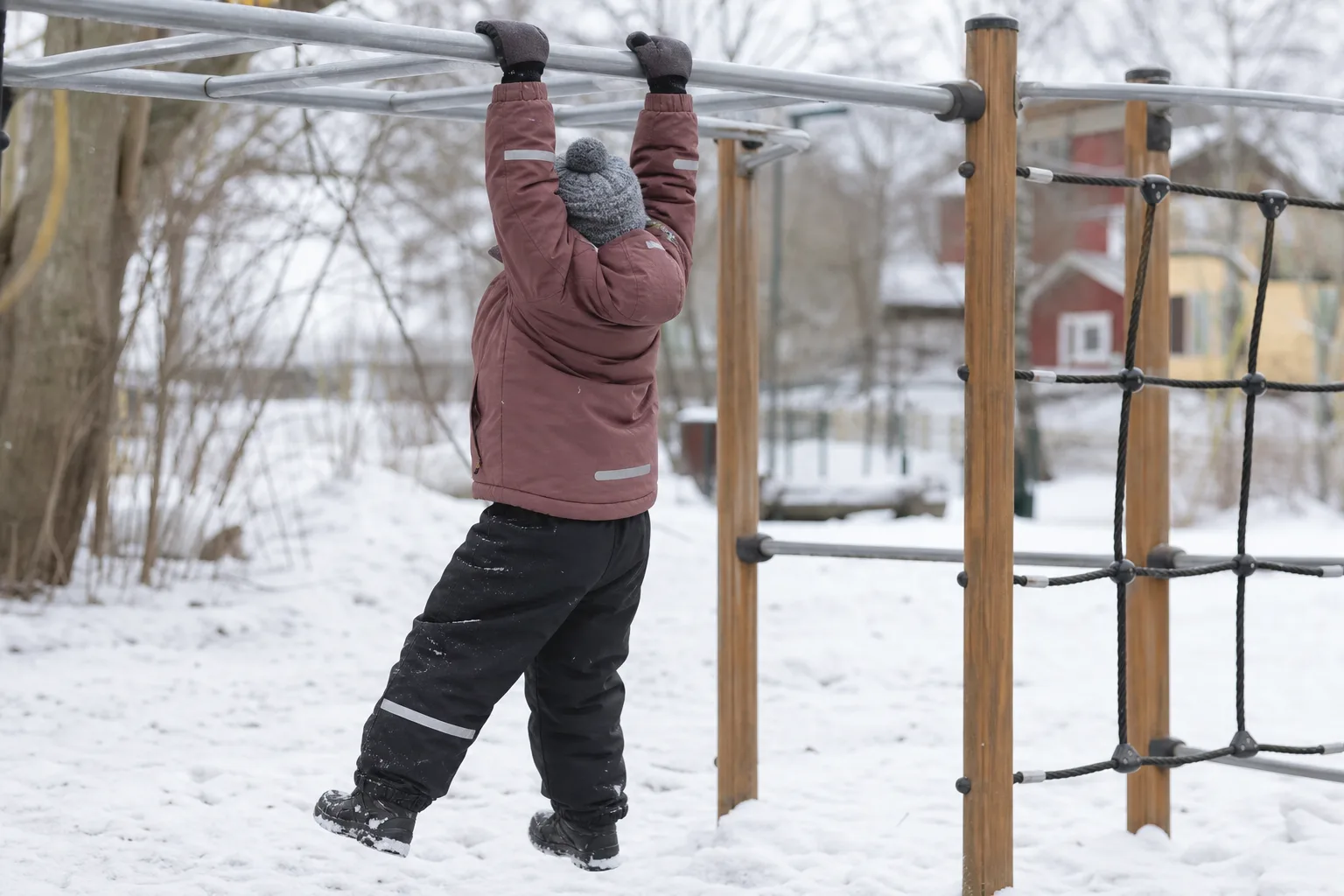 Barn i vinterjacka som sträcker armarna upp i en snöig lekpark