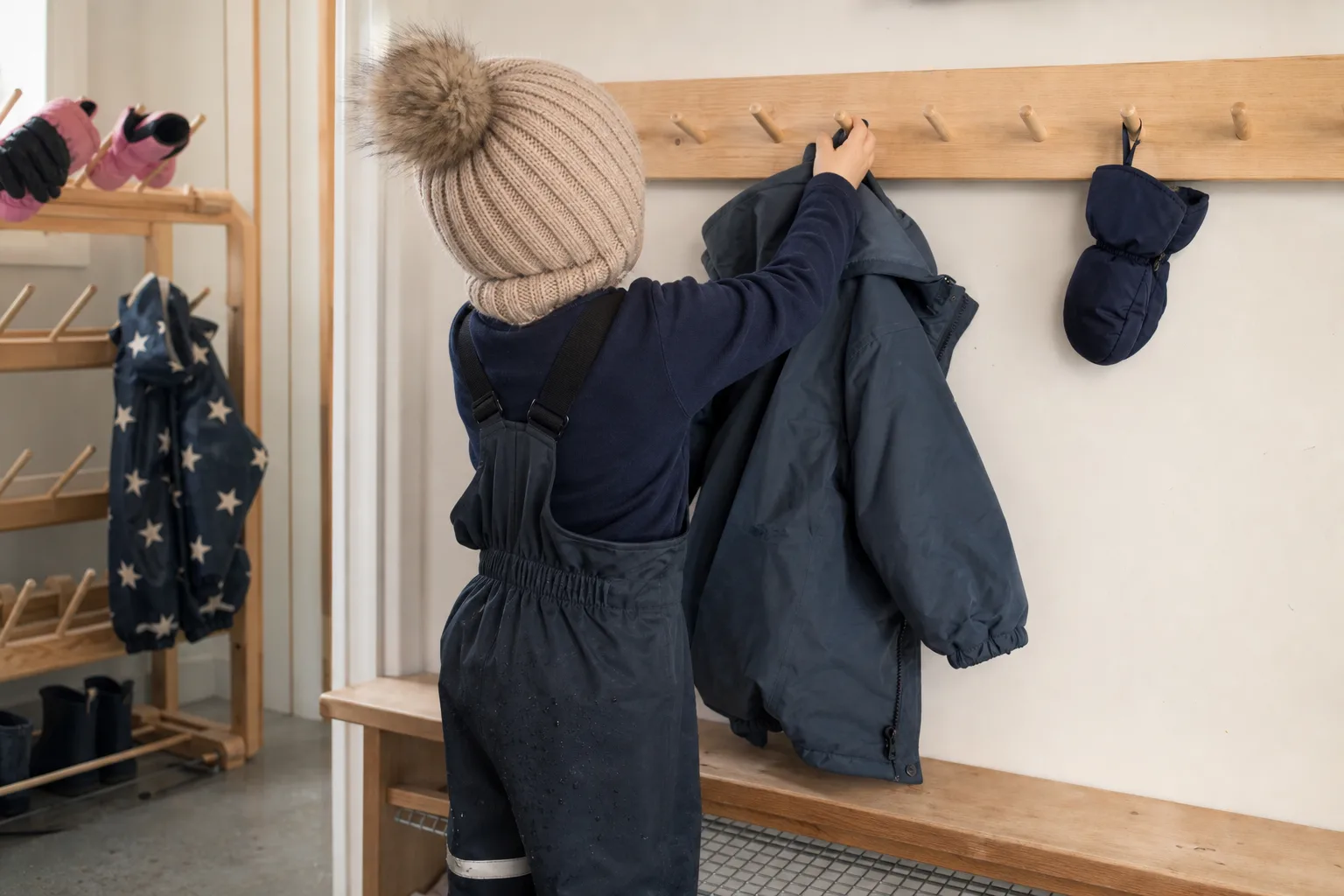 Barn sett bakifrån som hänger upp en vinterjacka i en förskolehall