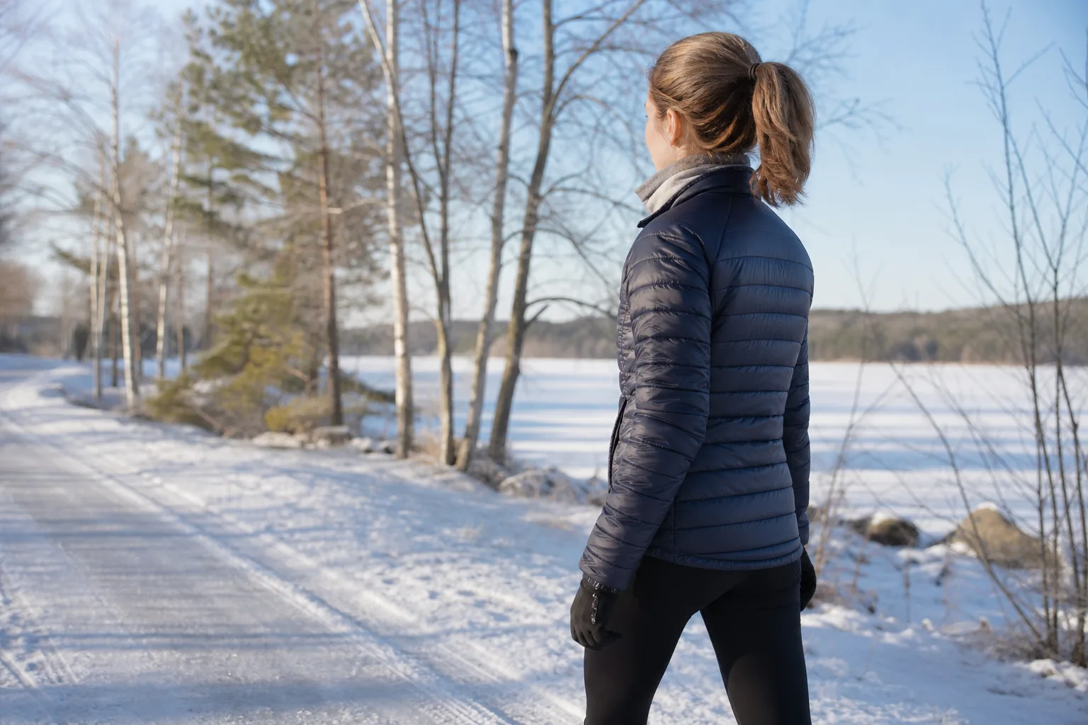 Kvinna i tunnare vinterjacka med lager vid halsen på en snöig vinterpromenad
