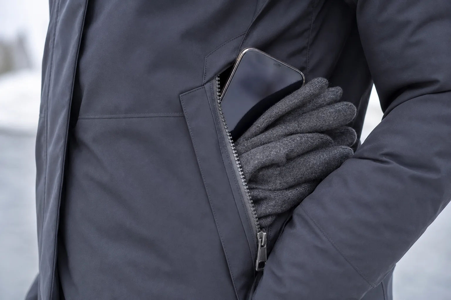Stor vinterjackficka med mobil och vikta handskar bakom delvis stängd dragkedja