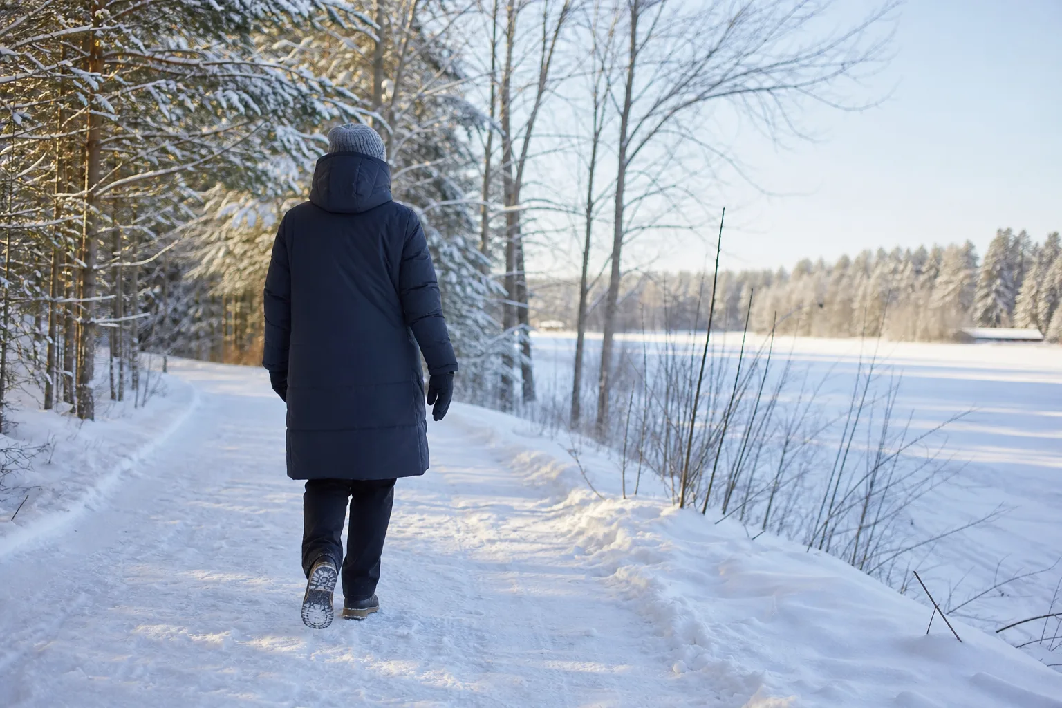 Person i längre vinterjacka på en snöig promenadväg i vinterlandskap