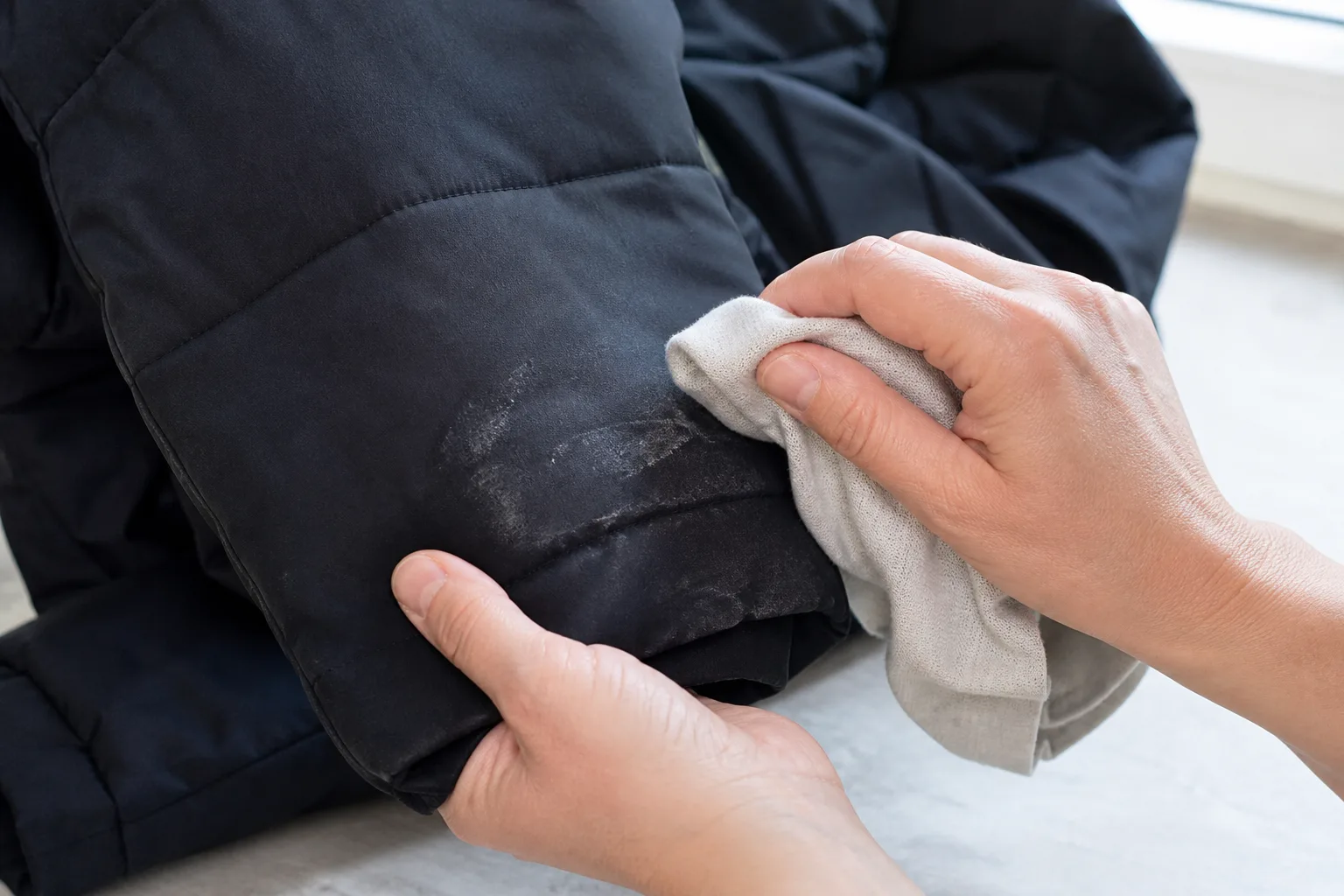 Händer som torkar bort en saltrand från en mörk vinterjacka med en mjuk trasa