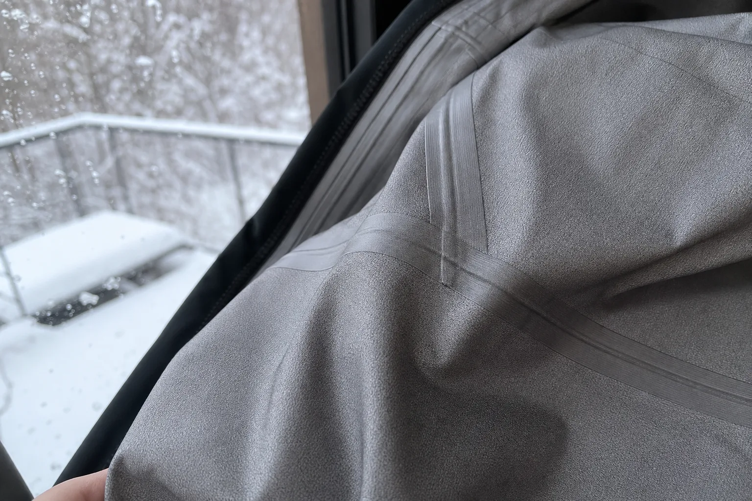 Tejpad söm på insidan av en vinterjacka vid ett snöigt fönster