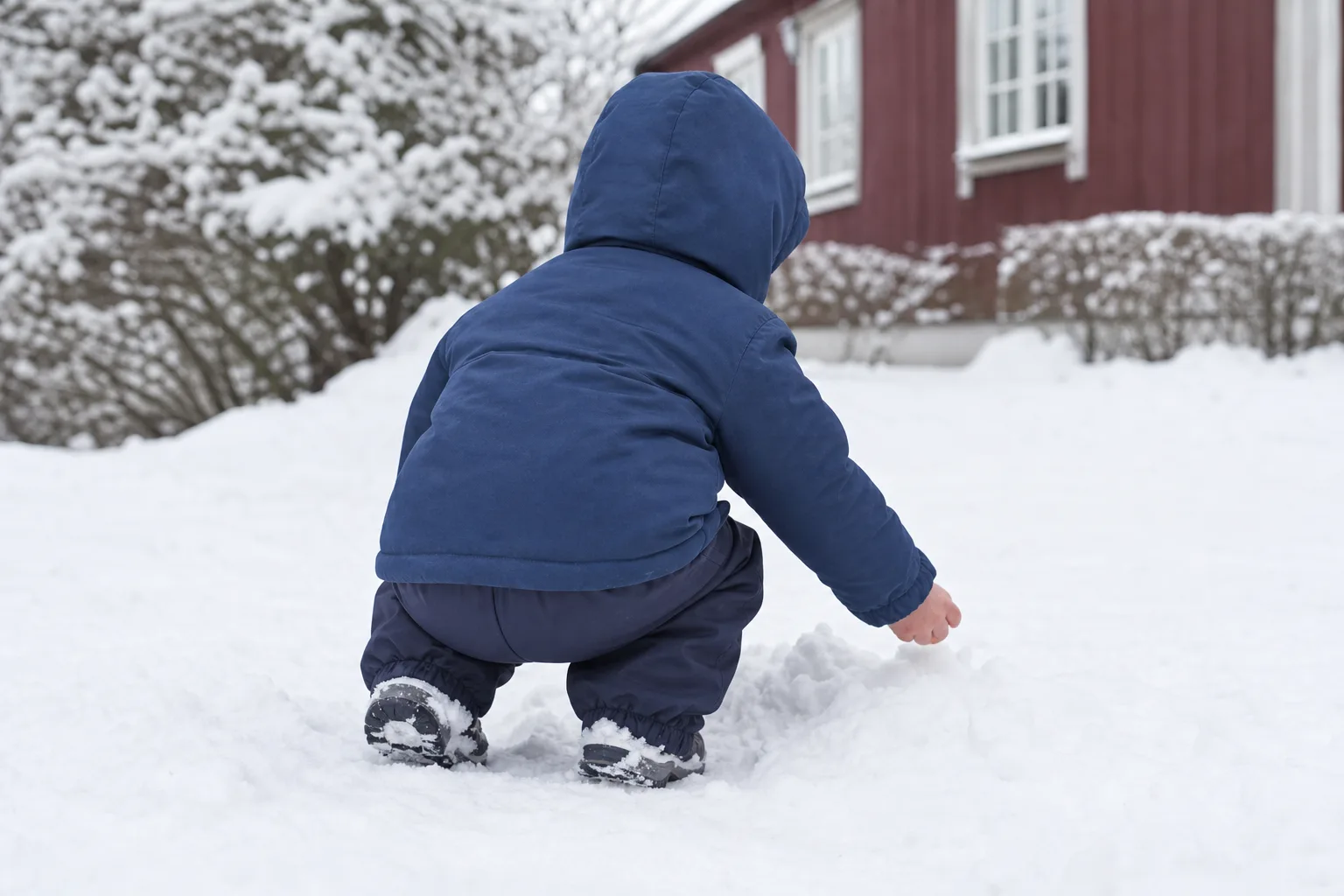 Barn sett bakifrån som hukar i snö med vinterjacka över separata termobyxor