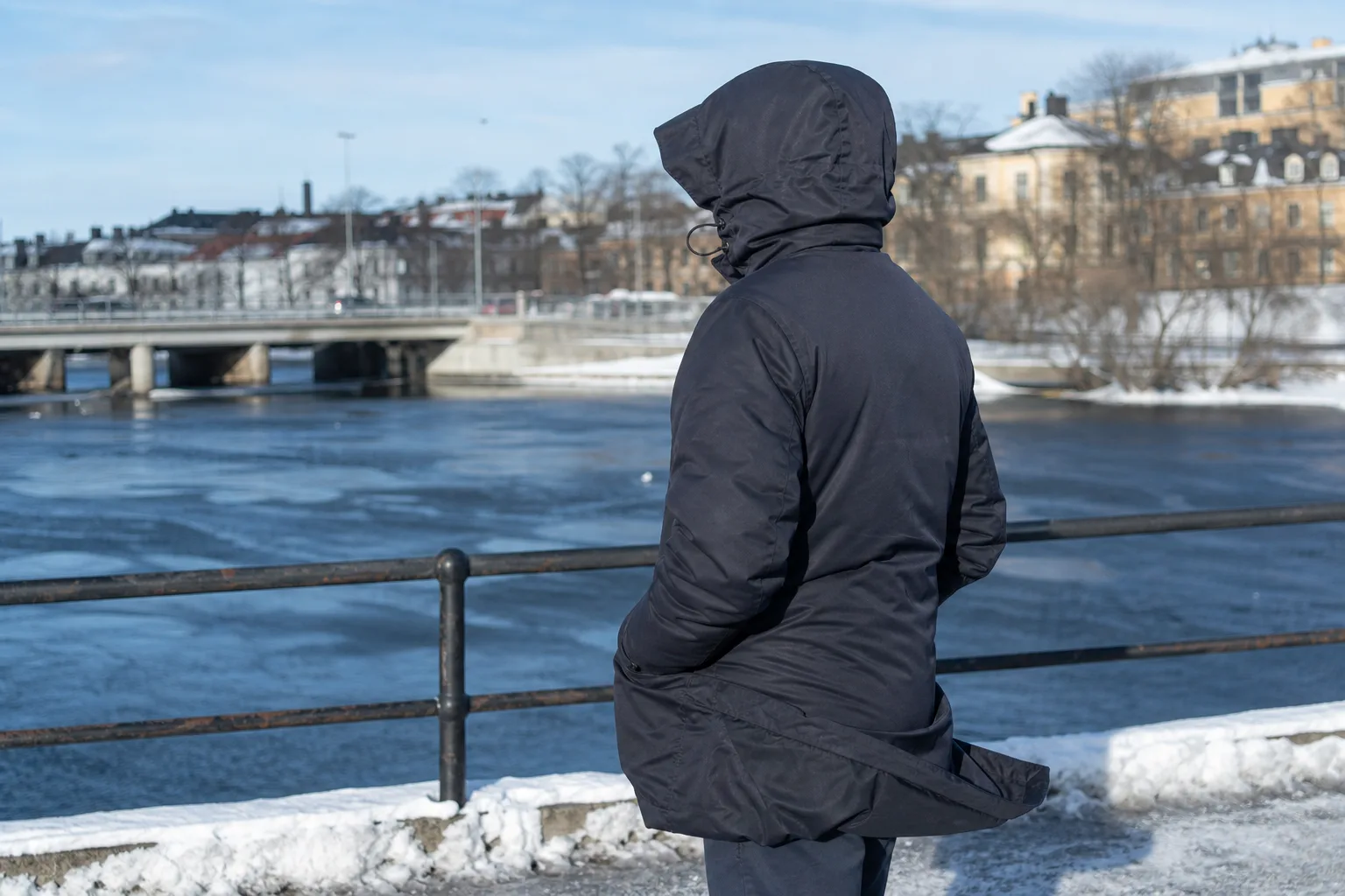 Person i lång vinterjacka med uppdragen huva vid en blåsig vinterälv
