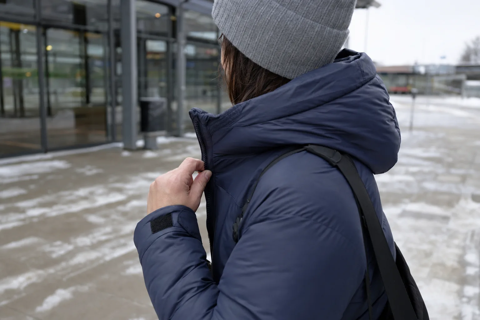 Pendlare som öppnar dragkedjan på sin vinterjacka utanför en station